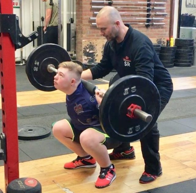 Coach Simon Roach spotting a young lifter performing a backsquat