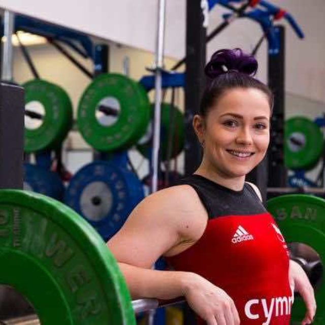 Christie Williams in Welsh Lifting suit smiles for a shot with a loaded weightlifting bar